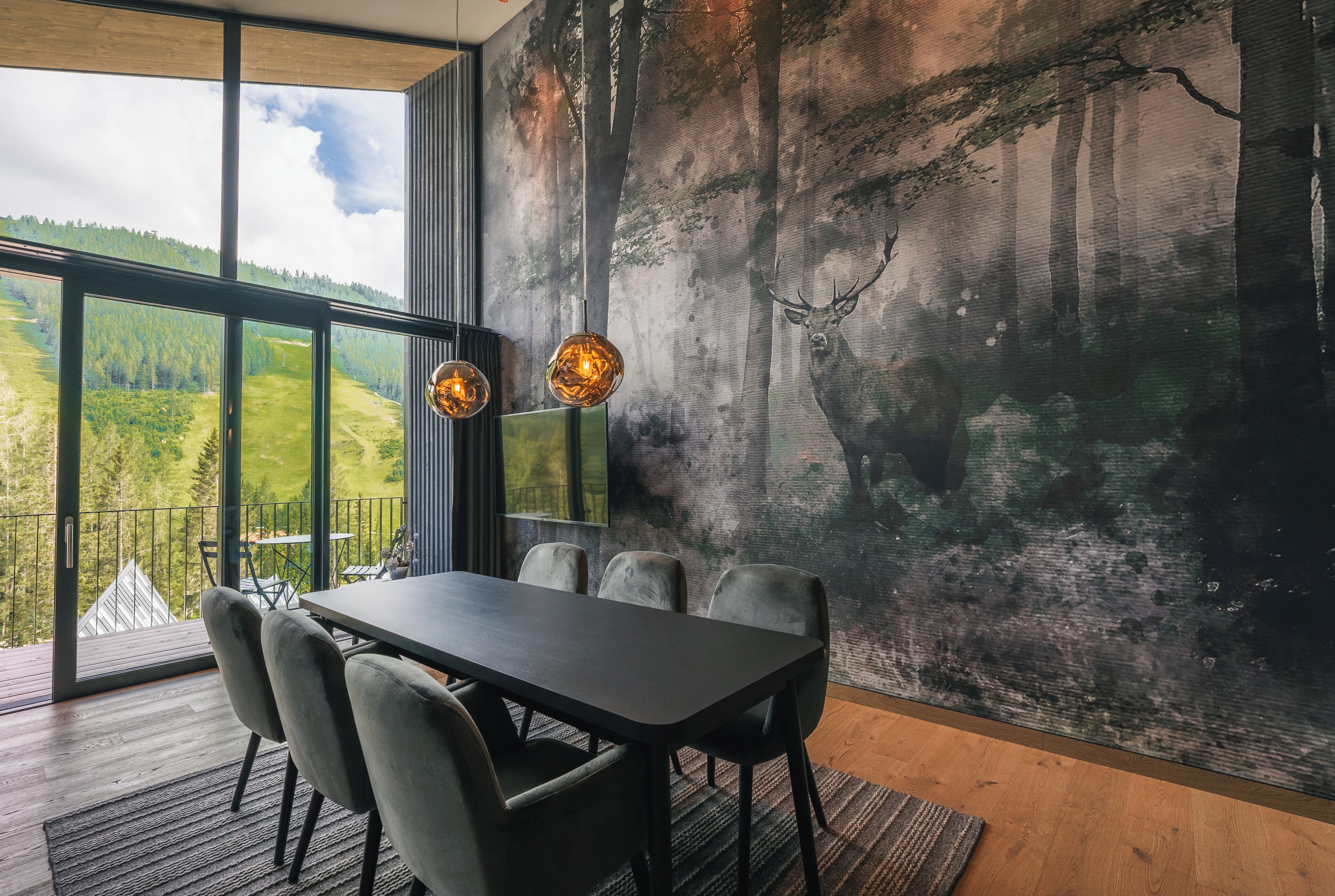A dining area with a table and chairs, a large window with a view of a forest, and a wall mural of a forest scene.