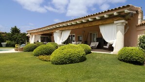Una villa con un porche cubierto, setos bien cuidados y una piscina.
