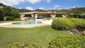 Una villa con piscina, rodeada de césped y setos cuidados, con montañas al fondo.
