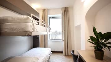 A compact hotel room with a bunk bed, a desk, a chair, and a potted plant.