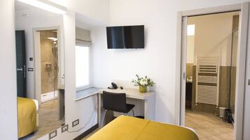 Une chambre d’hôtel avec un lit, un bureau et une chaise, une télévision et une salle de bain visible à travers une porte ouverte.