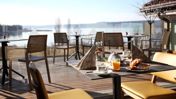 Un espace repas avec des tables et des chaises, une vue sur l’eau et une montagne en arrière-plan.