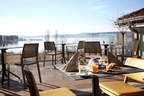 A dining area with tables and chairs, a view of the water, and a mountain in the background. - Hotel Ponti (Angera)