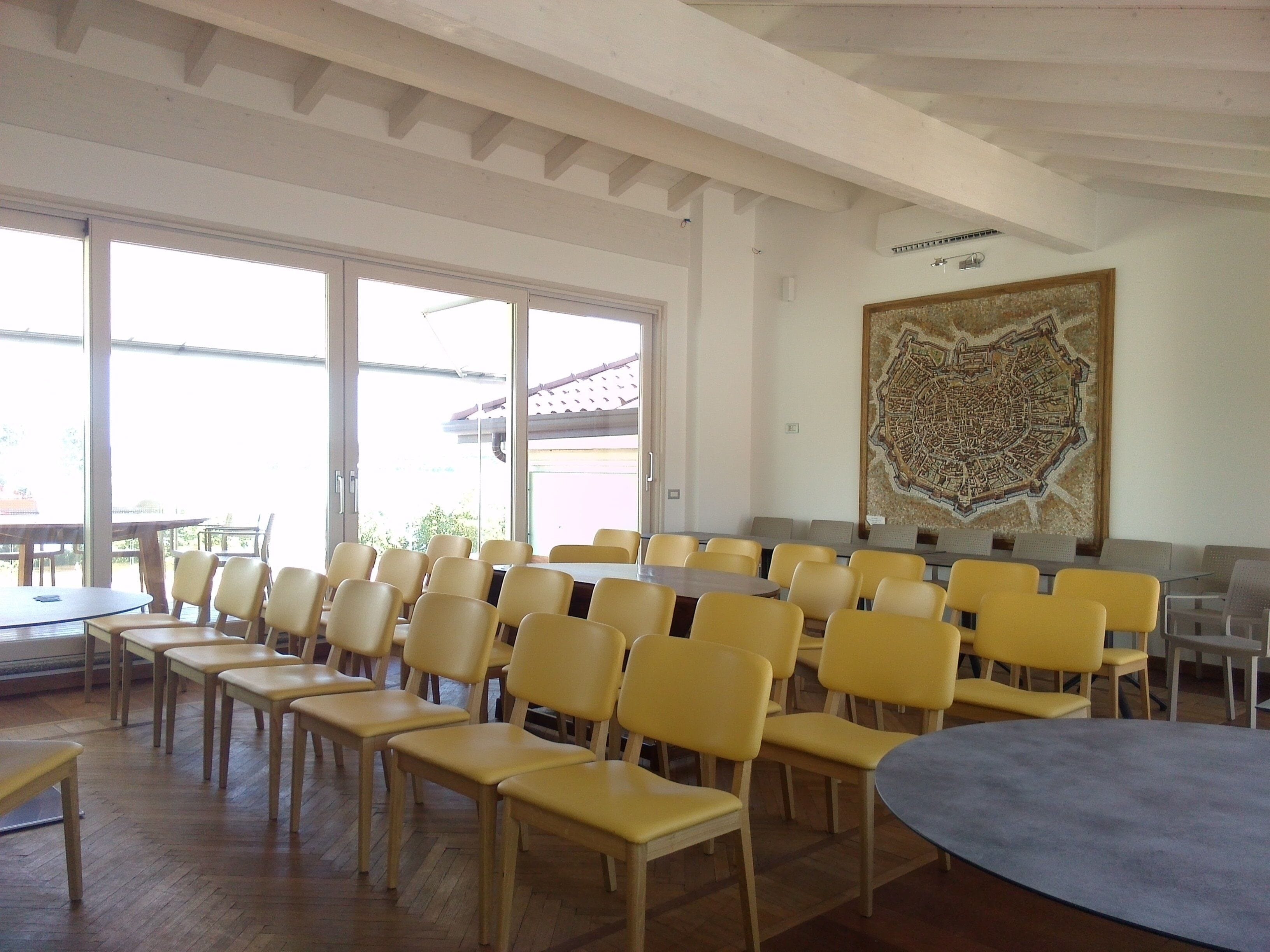 Un salón de conferencias con sillas amarillas, una mesa grande y una pintura de un paisaje urbano en la pared.