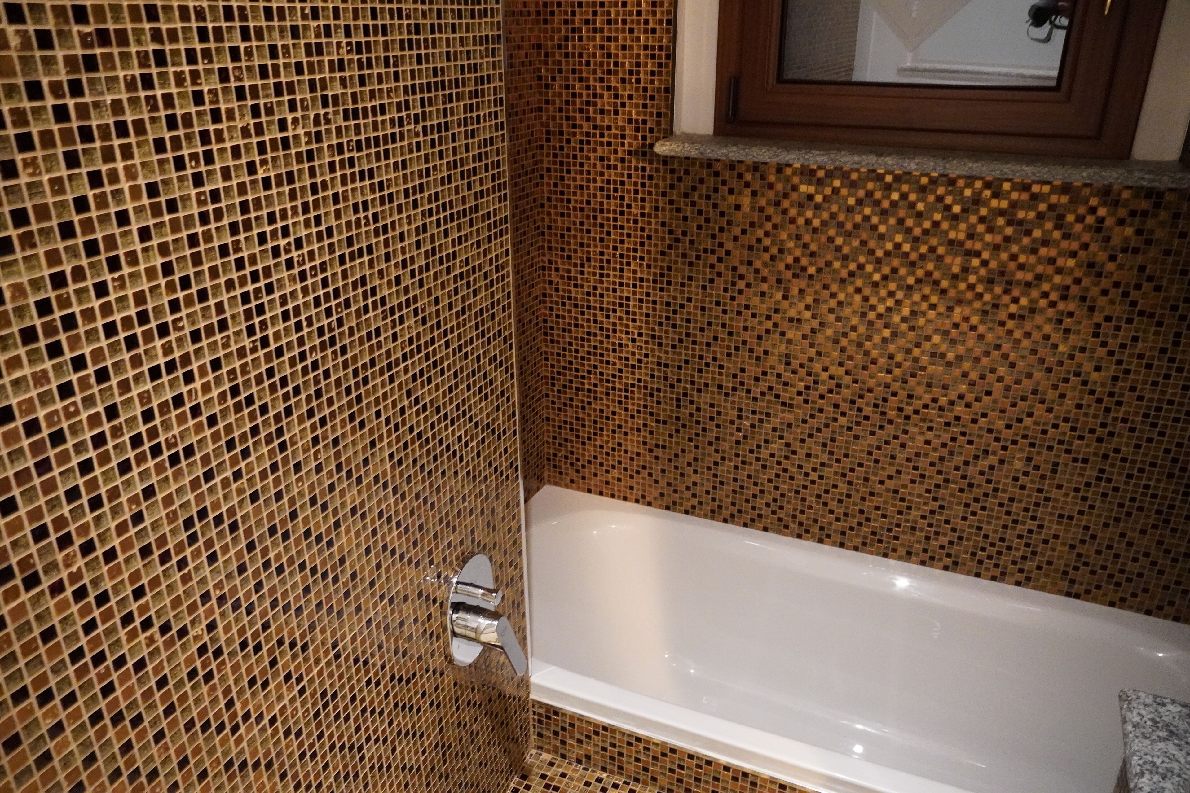 Ein Badezimmer mit Mosaikfliesen an den Wänden und einer weißen Badewanne.