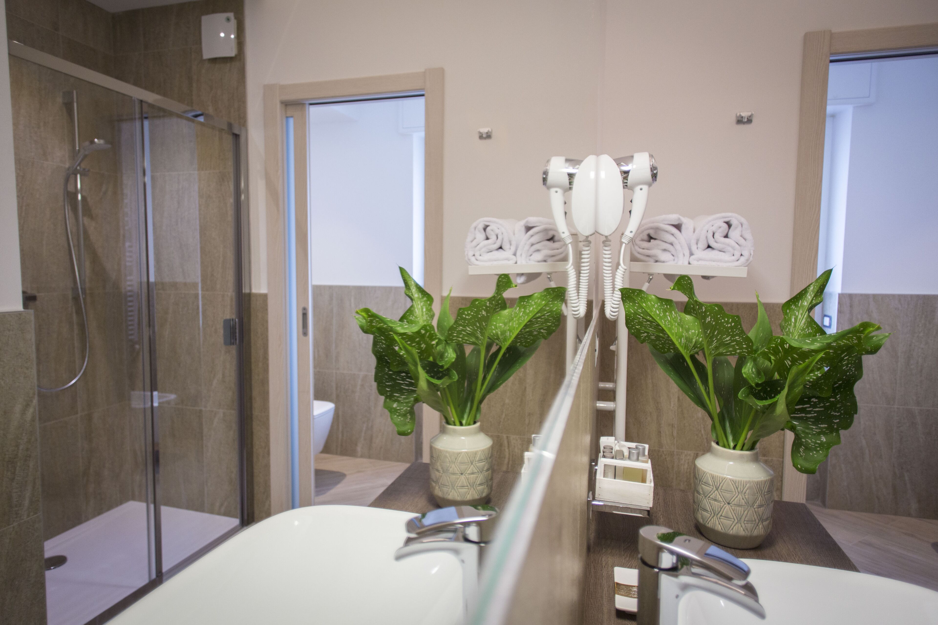 A modern bathroom with a glass-enclosed shower, a white sink, and two potted plants.
