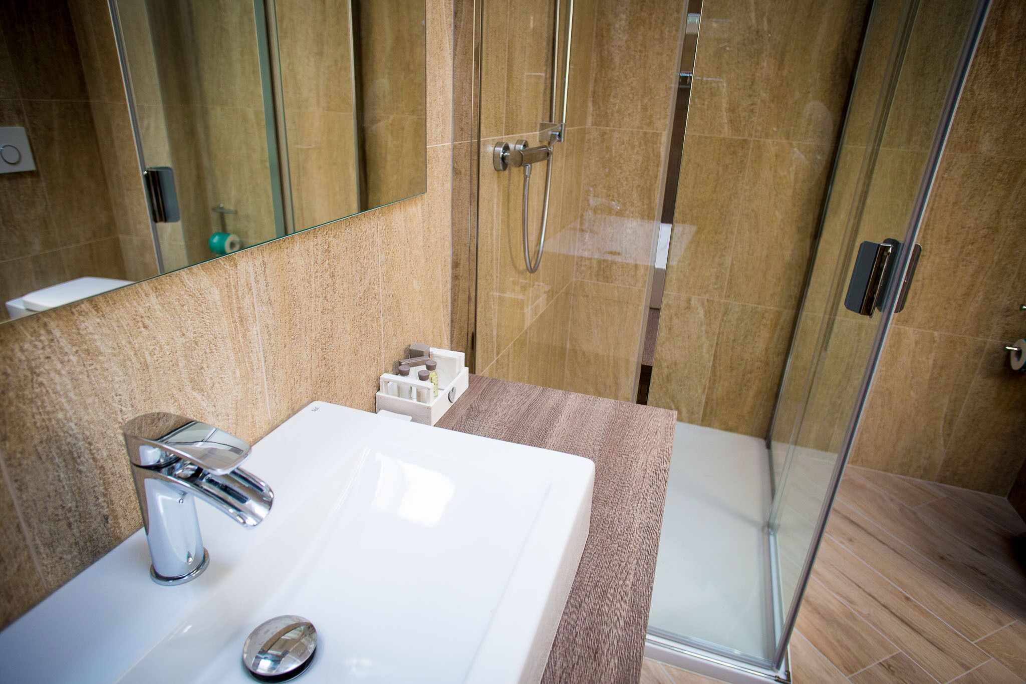 Une salle de bain avec un lavabo blanc, une cabine de douche en verre et un mur recouvert de carreaux de marbre.