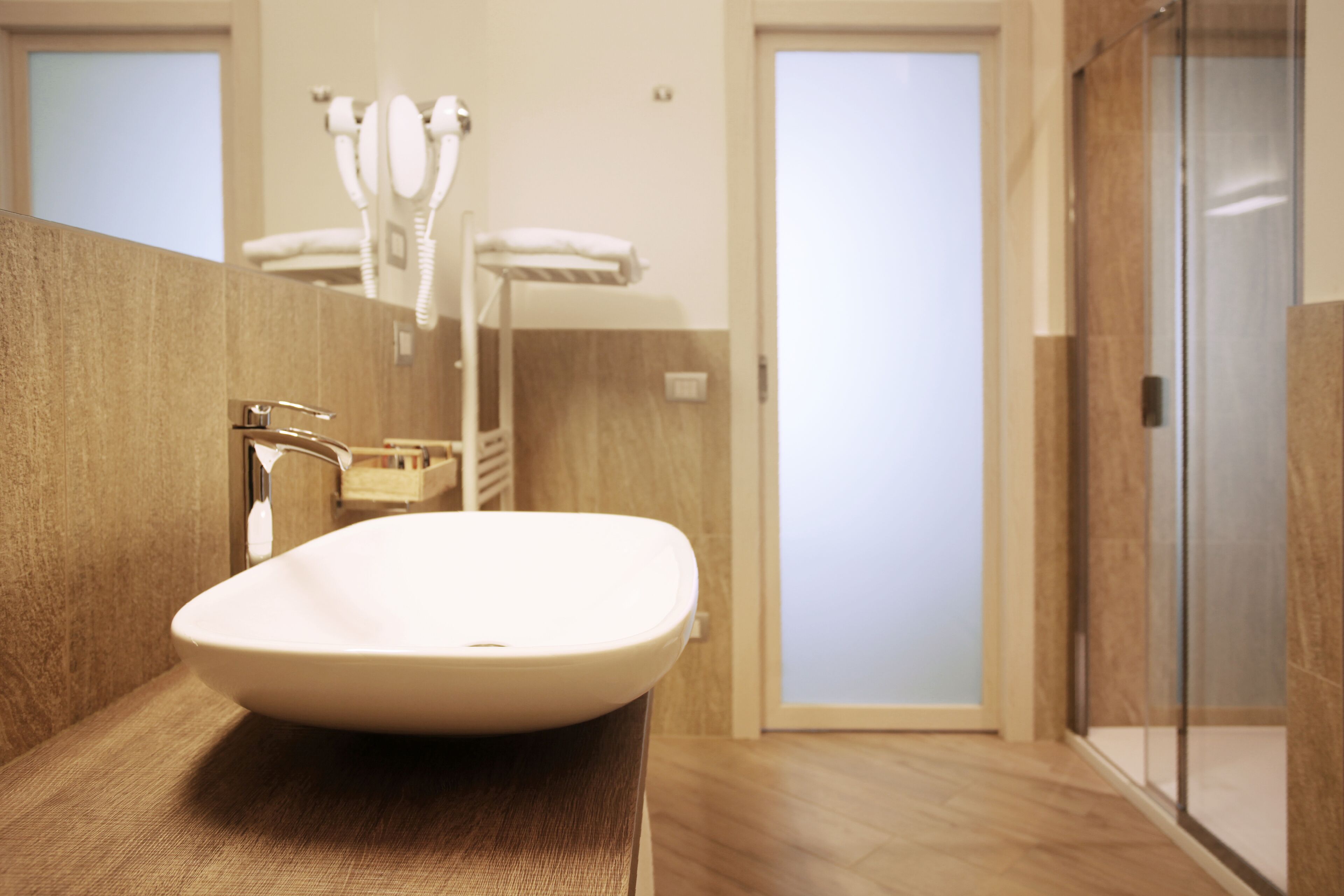 Un bagno moderno con un lavandino bianco capiente, un portascopevoli e una cabina doccia in vetro.