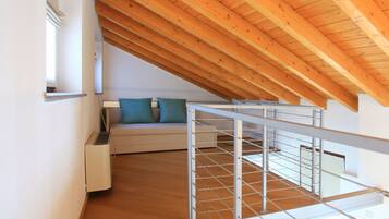 Ein modernes Schlafzimmer im Loftsstil mit schrägverlegtem Holzboden, einem weißen Sofa mit türkisfarbenen Kissen und einer Metalltreppe.