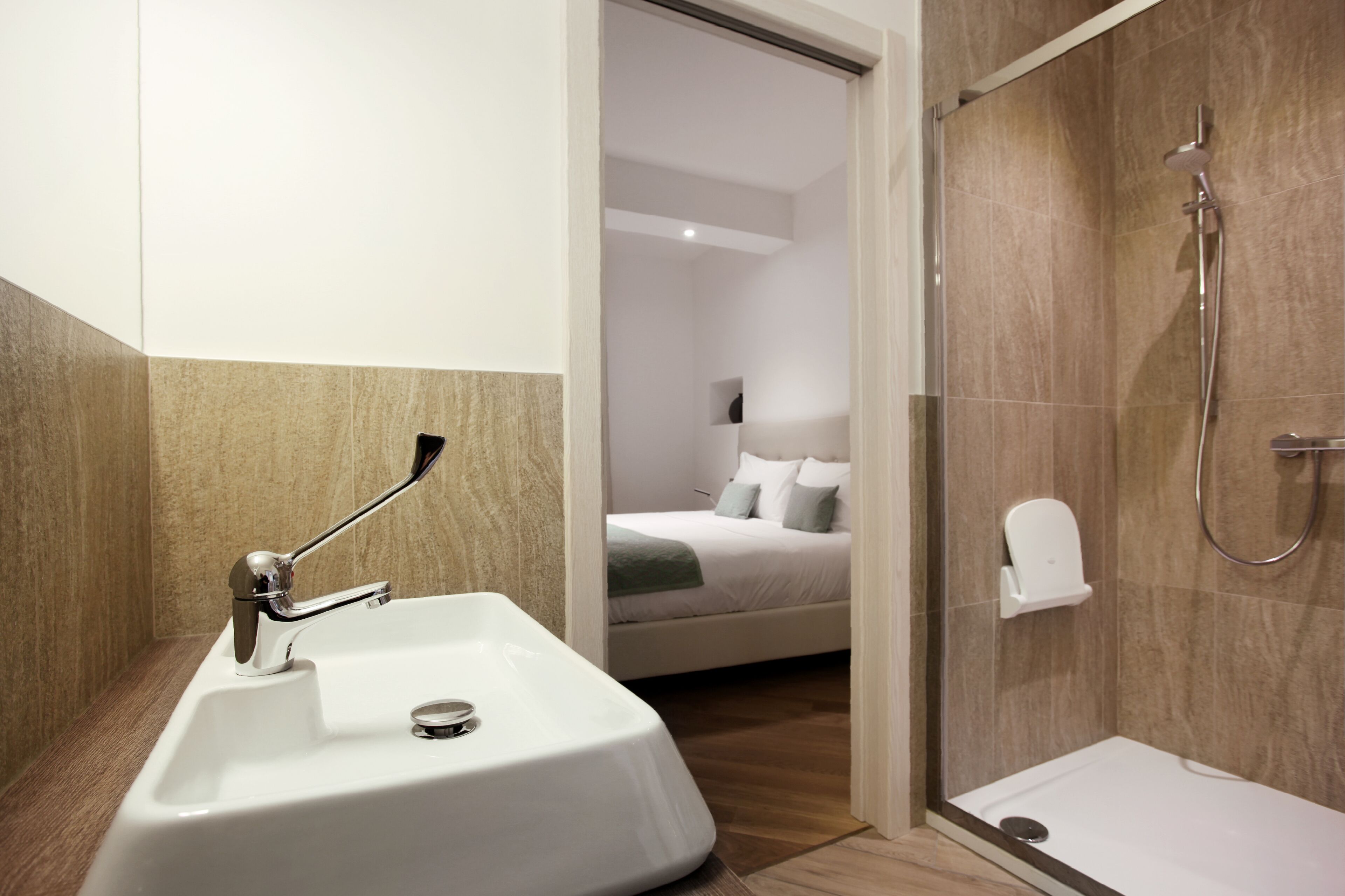 Un baño moderno con lavamanos, ducha y una habitación con cama y almohadas a la vista.