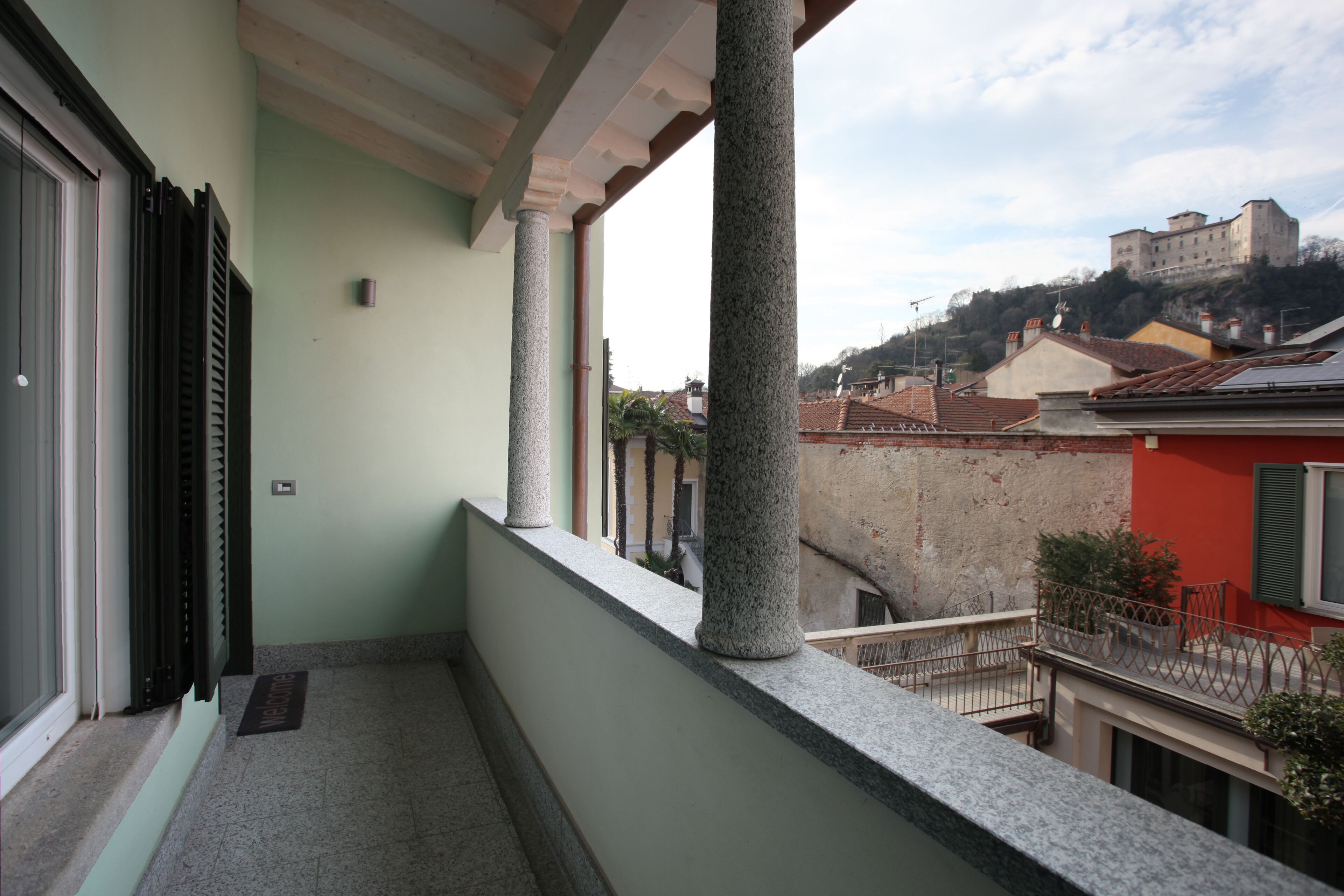 Un balcone con colonne in pietra, vista su una collina con un castello e un edificio rosso sullo sfondo.