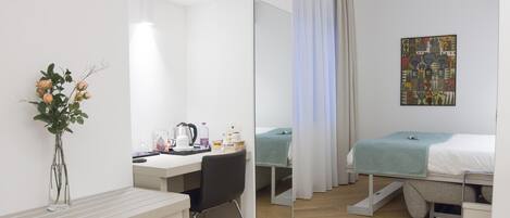 A modern hotel room with a desk, chair, and a bed with a teal blanket.
