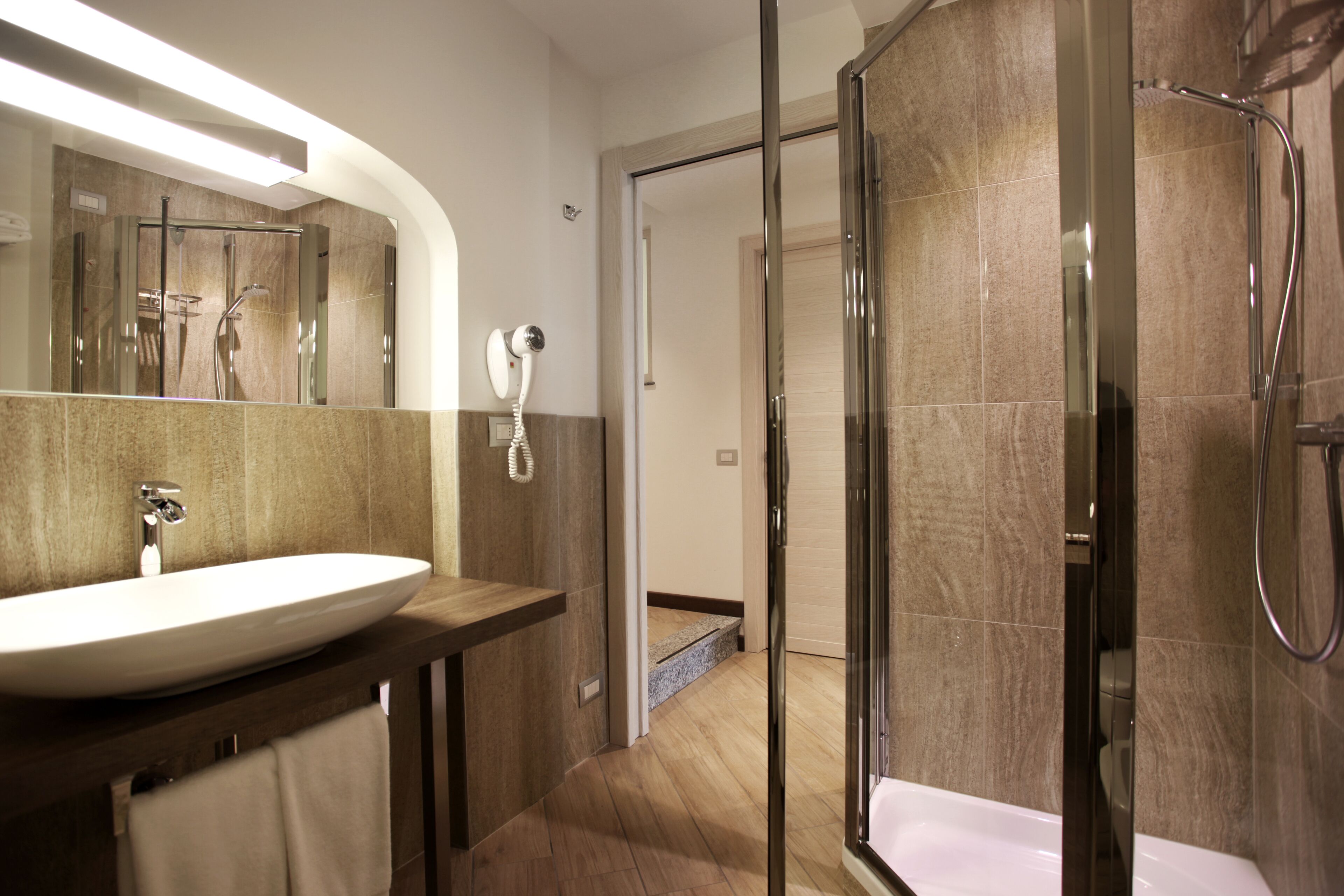 Une salle de bain moderne avec un grand lavabo, une douche en verre et une porte visible donnant sur une autre pièce.