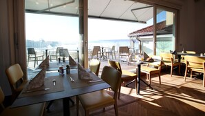 Un espace de restauration moderne doté de grandes fenêtres, d’une terrasse avec des sièges extérieurs et d’une vue sur la mer.