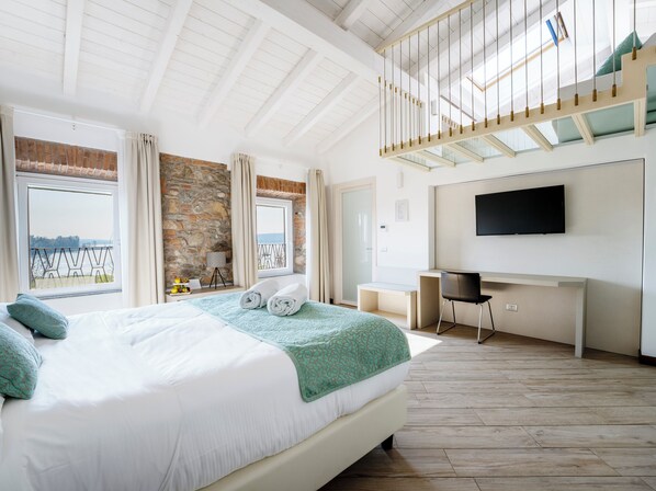 A bedroom with a large bed, a desk, a TV, and a balcony with a view. - Hotel Ponti (Angera)