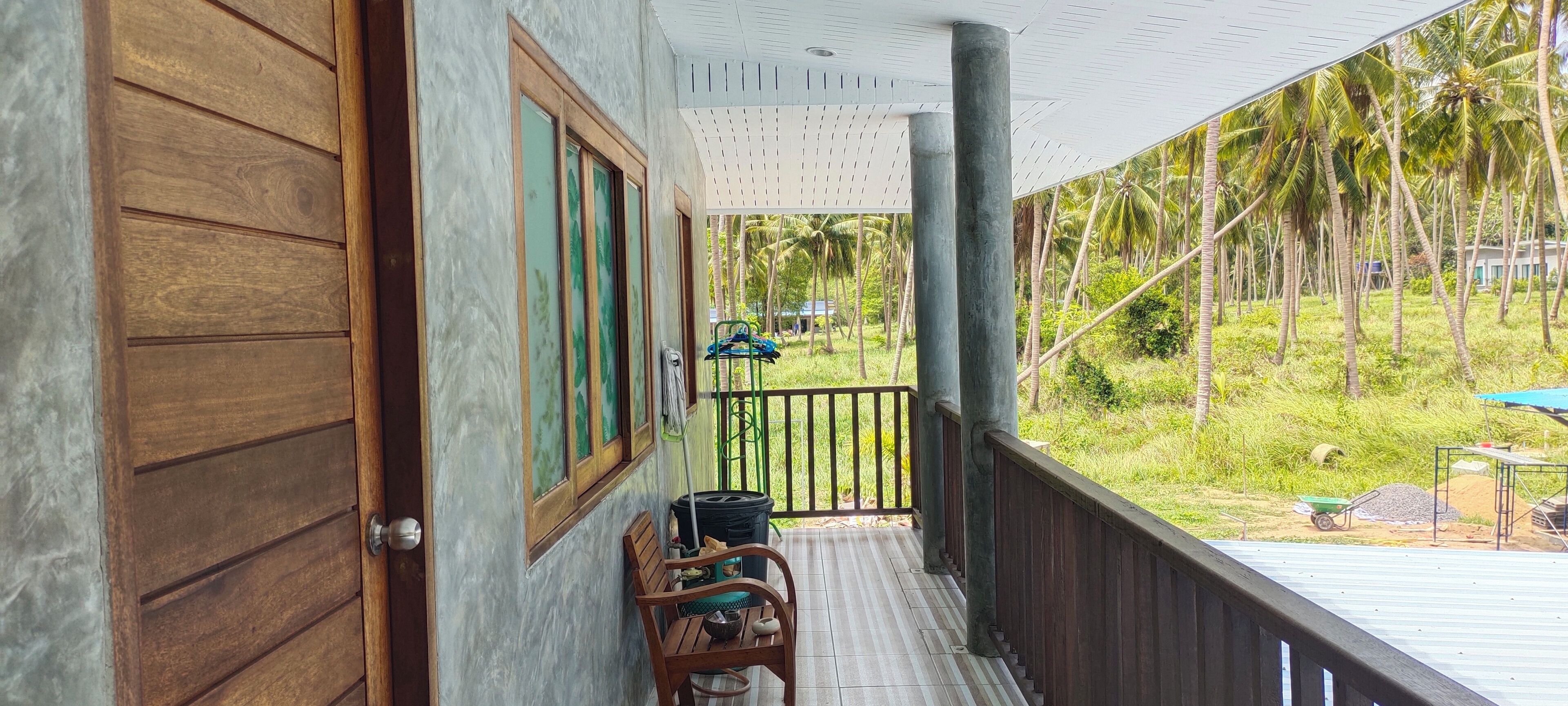 A wooden door, a window with a view of palm trees, and a balcony with a chair and a table.
