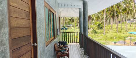 A wooden door, a window with a view of palm trees, and a balcony with a chair and a table.
