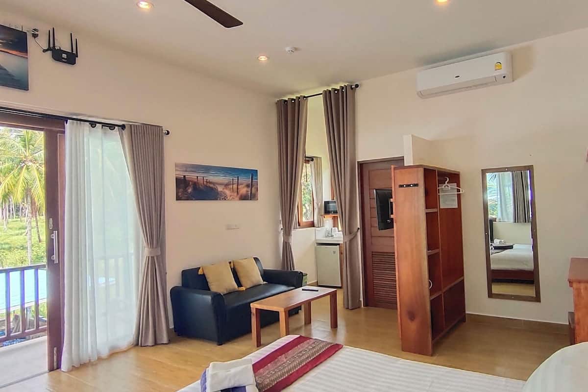 Una habitación con una cama, un escritorio de madera, un sofá negro, un armario de madera y un ventanal con cortinas.