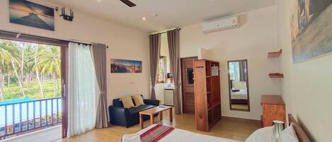 A room with a bed, a wooden desk, a black sofa, a wooden wardrobe, and a large window with curtains.