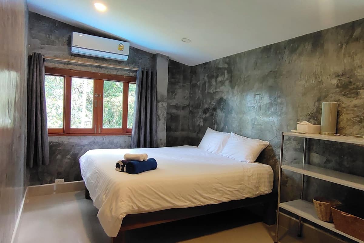 Un dormitorio con cama, ventana con cortinas, aire acondicionado y estante de metal con cestas.