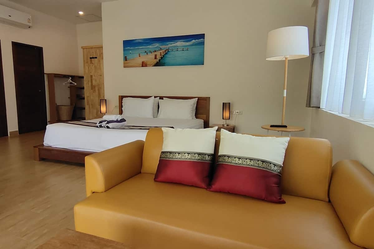Habitación de hotel con cama, sofá, un cuadro, lámpara y ventana con cortinas.