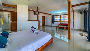 Amplia habitación de hotel con una cama grande, un área de descanso con un sofá rojo y vistas a la playa a través de las ventanas.