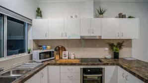 A modern kitchen with white cabinets, a microwave, a stove, and a dishwasher. - ZEN HIDEAWAY - Cozy 2BR Modern Unit (Alawa)