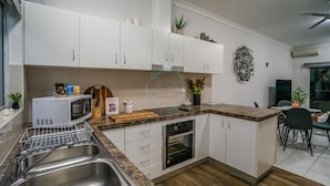 A modern kitchen with white cabinets, a microwave, a sink, and a wooden countertop. - ZEN HIDEAWAY - Cozy 2BR Modern Unit (Alawa)