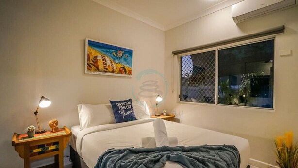 A bedroom with a large bed, two bedside tables with lamps, a painting on the wall, and a window with a view of the outside. - ZEN HIDEAWAY - Cozy 2BR Modern Unit (Alawa)
