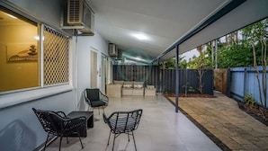 A covered outdoor area with a table and chairs, air conditioning units, and a view of the garden. - ZEN HIDEAWAY - Cozy 2BR Modern Unit (Alawa)