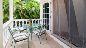 Ein Balkon mit Glastisch und Stühlen, einem Blumentopf und Blick auf üppiges Grün.