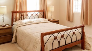Ein Schlafzimmer mit einem hölzernen Bett, zwei Nachttischen inklusive Lampen, einem Deckenventilator und zwei mit Vorhängen versehenen Fenstern.