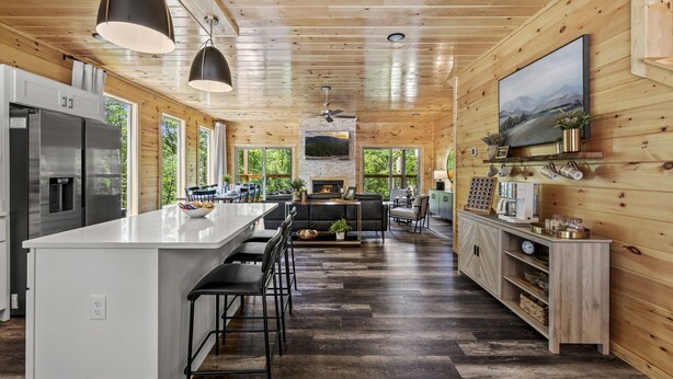 A modern kitchen with a central island, stainless steel appliances, and a dining area with bar stools. - Luxe Cabin|Indoor Pool~Game & Theater Rooms! (Sevierville)