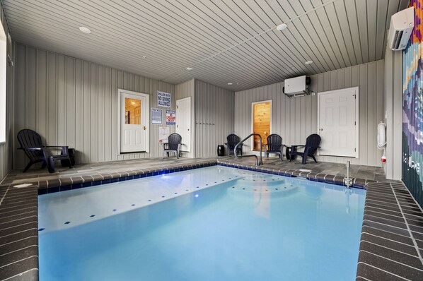 An indoor swimming pool with tiled walls and ceiling, surrounded by chairs and a door.