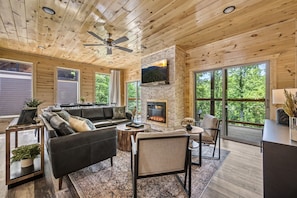 A spacious living room with a fireplace, large windows, and a ceiling fan.