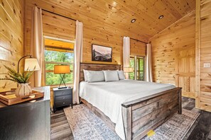 Une chambre dans une cabane en bois, avec un lit, des tables de chevet, une lampe et une fenêtre avec des rideaux.