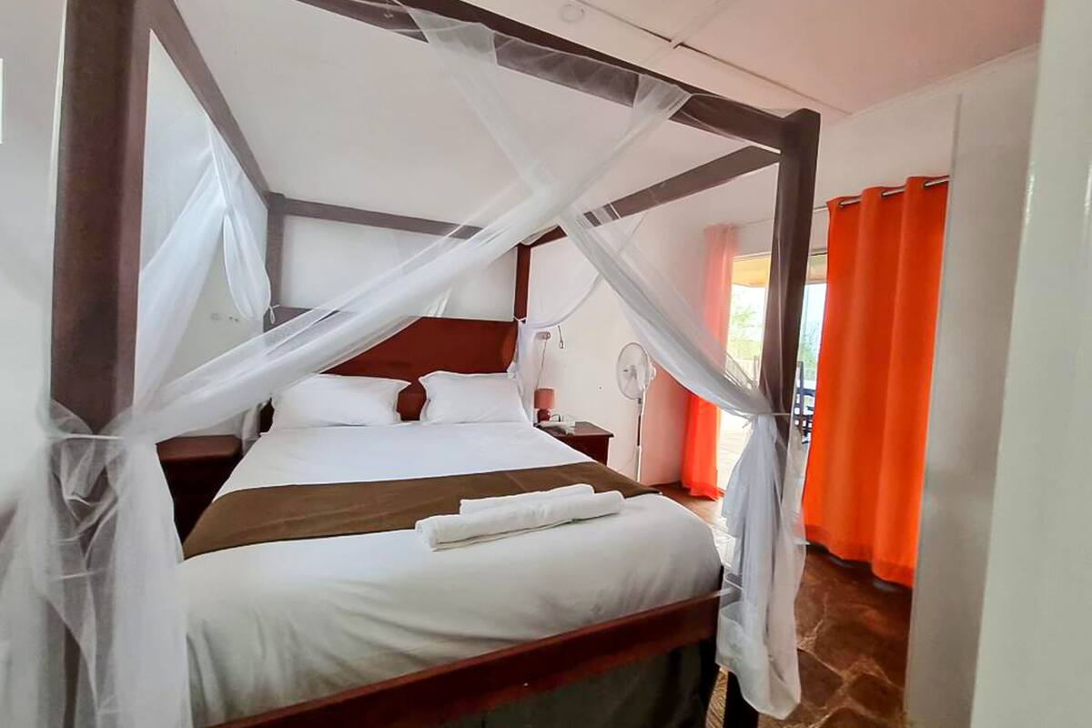 A four-poster bed with white linens, a wooden headboard, and a mosquito net.