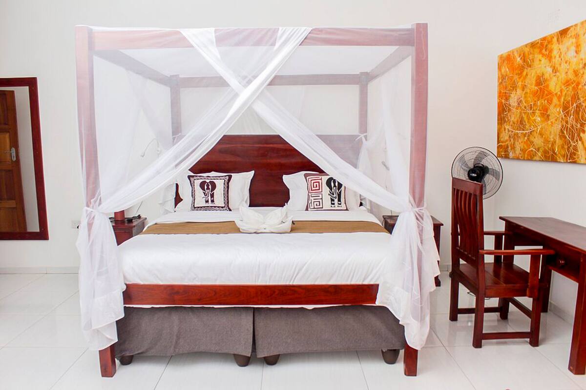A bed with a canopy, a bedside table, a chair, and a wall-mounted fan.