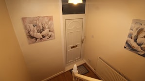 Un passadís amb una porta blanca, un radiador i dos quadres florals a les parets.