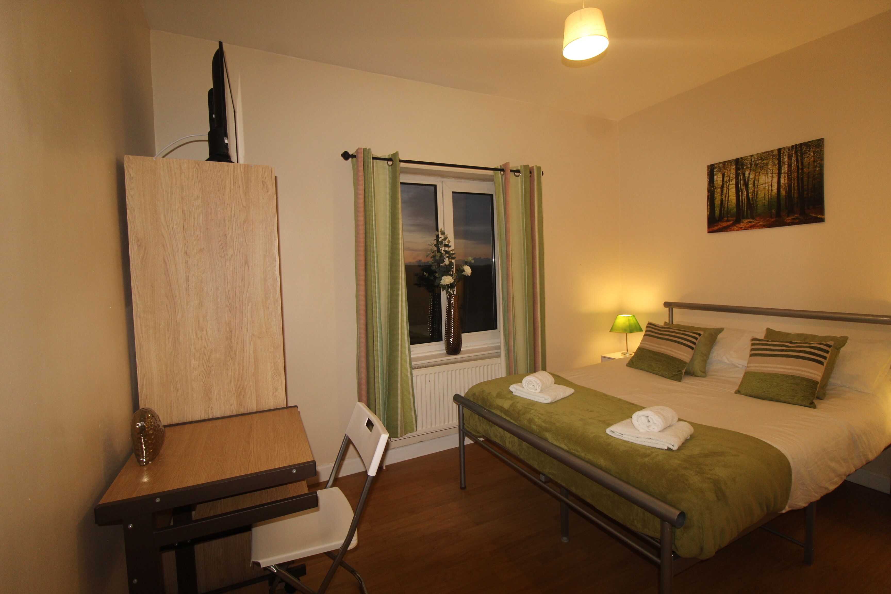 Una camera da letto con un letto, una scrivania, una sedia, una finestra con tende, un quadro appeso al muro e una lampada.