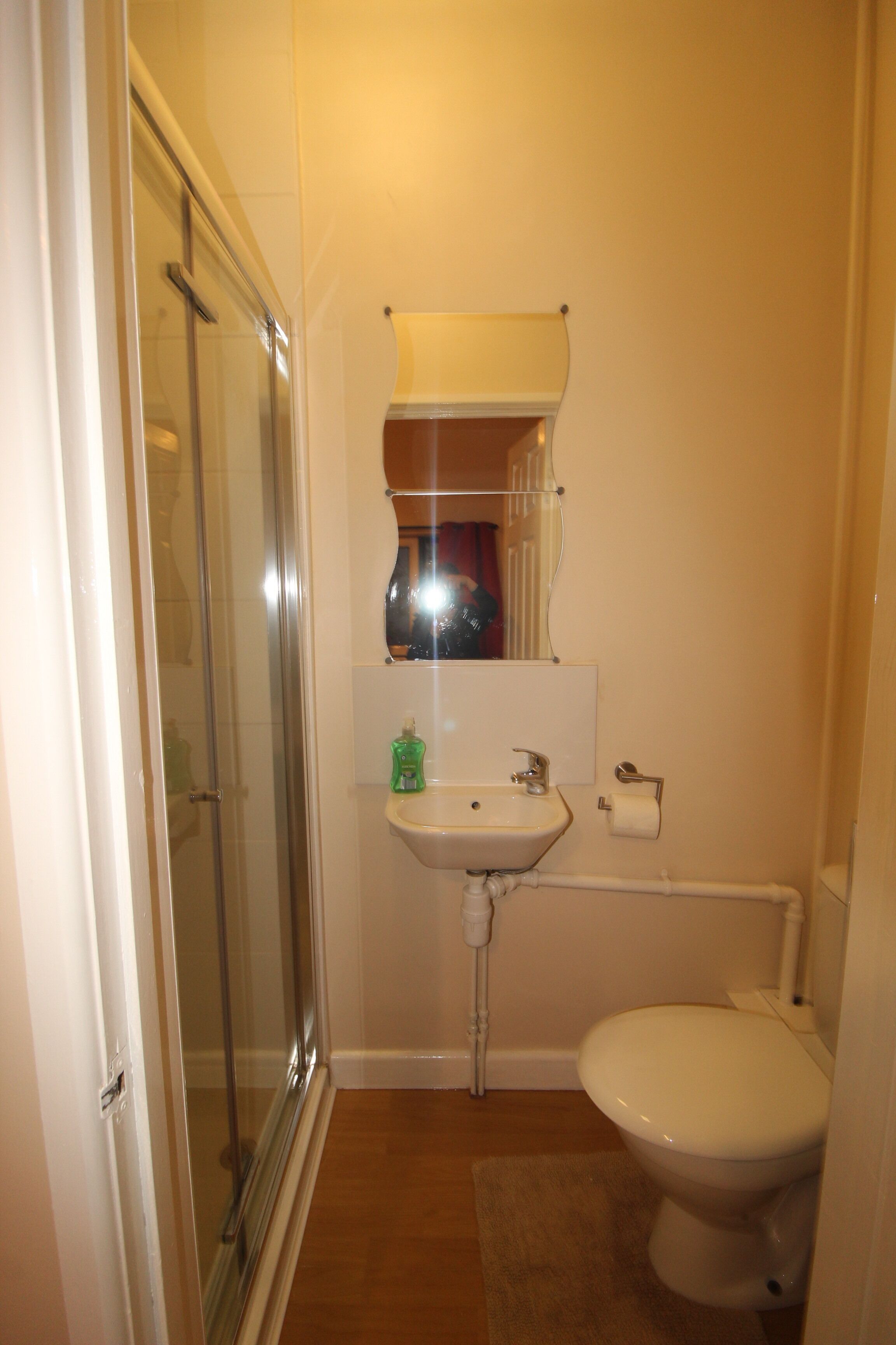 A compact bathroom with a glass shower enclosure, a pedestal sink, and a toilet.
