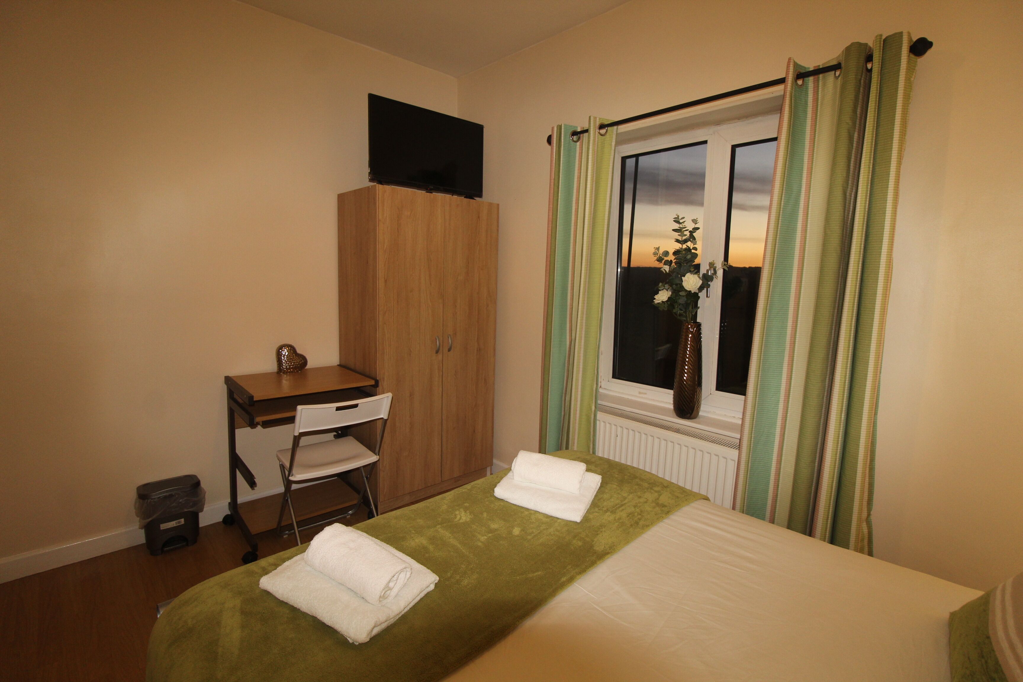 A hotel room with a bed, a desk, a chair, a TV on a cabinet, and a window with curtains.