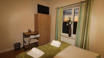 A hotel room with a bed, a desk, a chair, a TV on a cabinet, and a window with curtains.