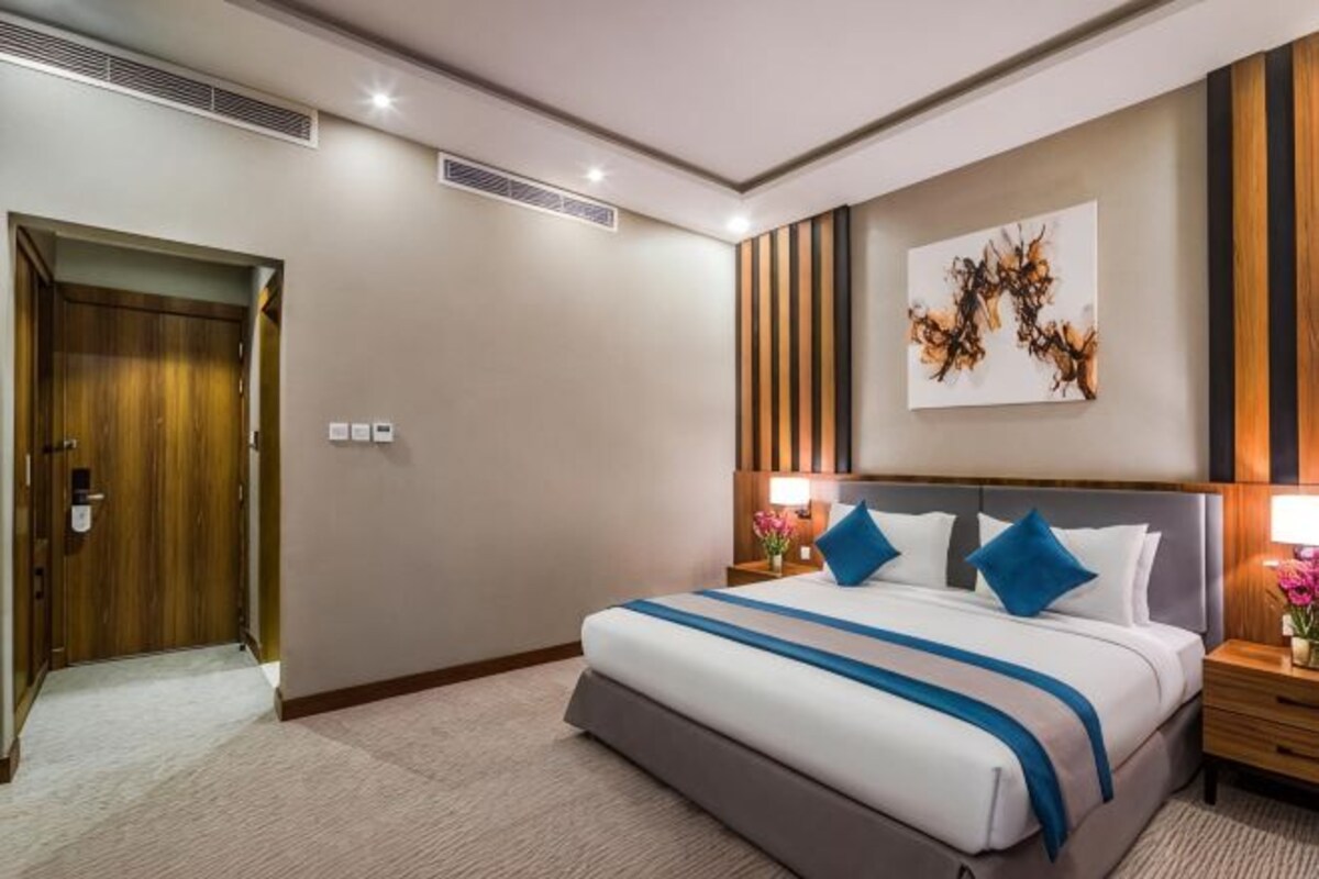 Ein Hotelzimmer mit einem großen Bett, Nachttischen, einer Tür und einem an der Wand hängenden Kunstwerk.