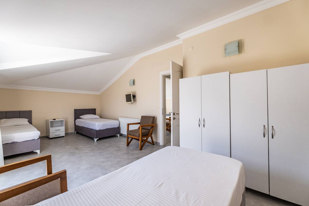 Ett sovrum med två sängar, en stol, en garderob och ett litet nattduksbord.