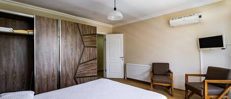 Quarto de hotel com uma cama, duas cadeiras de madeira, uma TV, ar condicionado e um guarda-roupa.