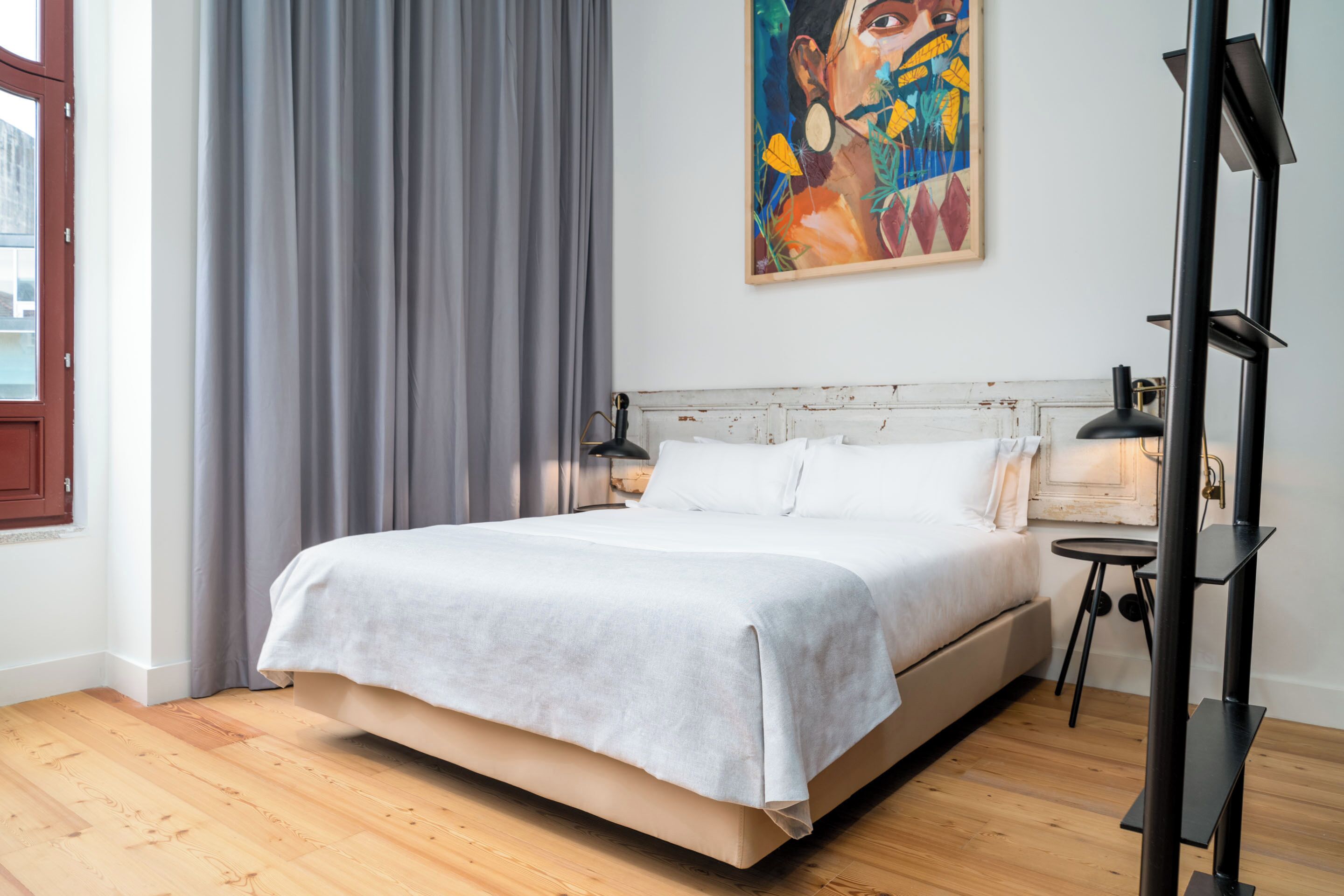 A modern bedroom with a large bed, a bedside table, a lamp, and a painting on the wall.
