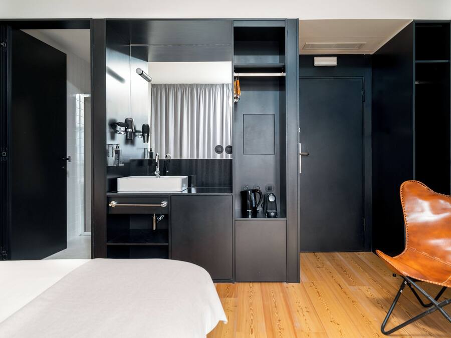 Una habitación de hotel moderna con cama, escritorio integrado, lavabo, espejo y armario.