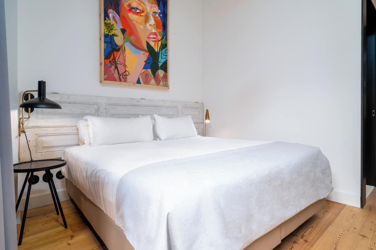 Un dormitorio con una cama grande, una mesita de noche, una lámpara y un cuadro en la pared.