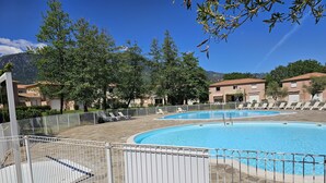 A swimming pool with a white fence, lounge chairs, and buildings in the background. - Villa Melody Calme DS Residence Securisee Avec Piscines Proche MER ET Montagne (Santa-Maria-Poggio)